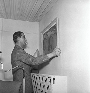 In the 1940s. A man tries to put a painting up on the wall and is carefully adjusting it so it hangs right