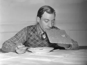 1940s meal. A young man, athlete Erik Pettersson at the food table taking a bite from the bread