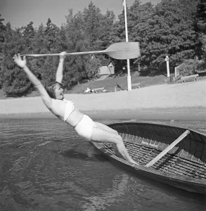 1940s summer. A young woman has made attempt to stand up in a wonky canoe