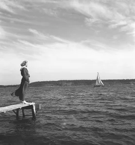 1940s summer. A young woman is standing by the seaside as she is waiting for something