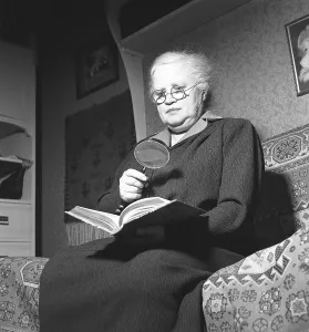 1940s woman with glasses. An older lady is looking in a book using both glasses and a magnifying glass