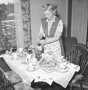 In the 1940s. A woman has set a table for Easter and arranges daffodils to be placed in a vase on the table