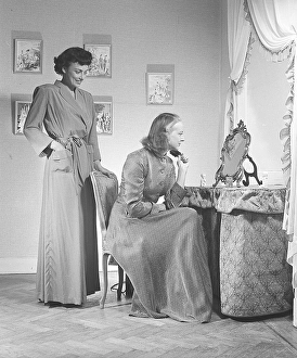 1940s women at home. A woman is sitting by a make up table looking at herself in the mirror whire brushing her hair
