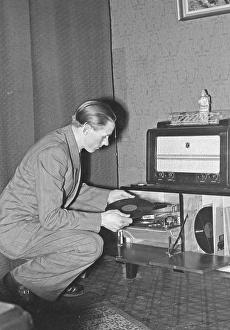 In the 1940s. World champion runner Gunder Haegg, 1918-2004, from Sweden pictured in his home while listening to music records on hthe gramophone. He also has a nice radio.1942