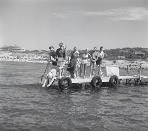 1950s on the beach. Sunny day by the seaside and people standing looking when a woman dives into the water