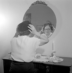 In the 1950s. A lady looks her self in the wall mirror to see that her hat looks good on her. Sweden 1952 ref Conard 3160