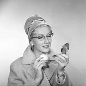 1950s makeup. A woman is looking at herself in her pocket mirror and improves on her makeup