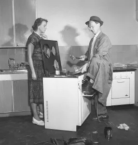 In the 1950s. A man at an electric cooker from swedish manufacturer Husqvarna, doing some work on the stove looking very non-professional.A woman is standing on the side looking at him in a skeptical manor. Sweden 1950. Kristoffersson ref AZ69-12
