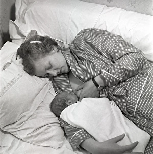 1950s mother nursing her baby. A young woman breastfeeding her baby while lying in bed at home
