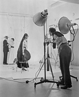 1950s photographer and models. A young woman is dressed up as to be being on a masquerade party with her eyes covered and spanish clothes. In the background a Zorro-looking man dances with a woman. Sweden 1957
