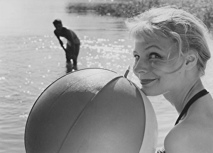 1950s summer. A young blonde woman looks into the camera holding a typical ball to use when playing on the beach with