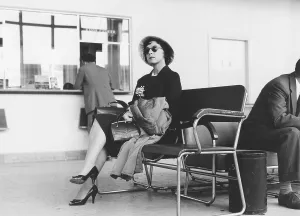 In the 1950s. A woman in focus is sitting in the terminal building in Bromma airport Stockholm Sweden. She is waiting to depart with an airplane and sits on a bench and waits comfortable but ready, having her carry-on bag and handbag close