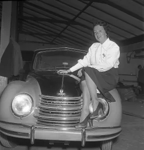 In the 1950s. A young woman on the hood of the brand new car