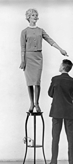 In the 1950s. A young woman seen standing on a piece of furniture higher than the man standing next to her