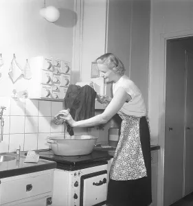 This is how it was done in the 1950s. A young woman stands at the kitchen sink and uses Bouvy salt with iodine to dye or wash her clothes. She rinses with clean water and looks pleased with the result. 1951. Kristoffersson ref BB68-2