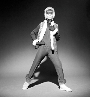 In the 1960s. A fashion model, in typical 1960s winter clothes in a studio. She has a thin overall on top over a knitted long sleeved sweater together with a vest, gloves and cap. Sweden 1966