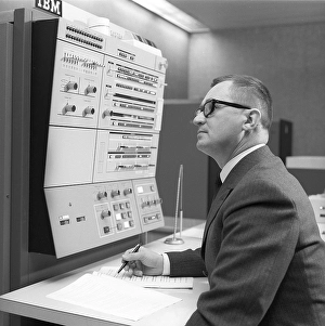 In the 1960s. Interior of a room with computers and people on the job of handling them and register and reading information. A sign above the mainframe computer says IBM 360
