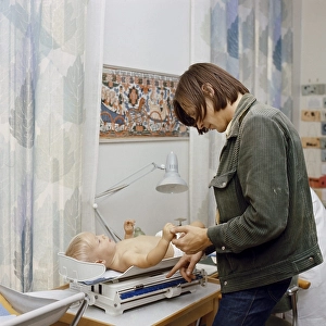 1960s parents. A father at the childcare center is checking the weight of his son who is lying on the scales. 1969