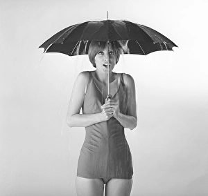 1960s woman. A young woman in a bathing suit is standing under an umbrella