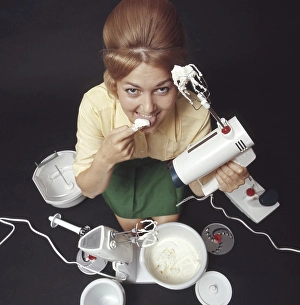In the 1960s. A young woman pictured with an electric mixer having whipped cream and is tasting it. She is dressed in the typical 1960s colors of clothes and her hair in the popular Beehive hairdo. Sweden 1969. Kristoffersson