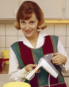 In the 1960s. A young woman pictured in the kitchen using an electric hand mixer