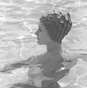 In the 1960s. A young woman pictured in the swimming pool wearing a typical 1960s bathing cap in a plastic material