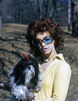 1970s glasses. A young woman in blue tainted sunglasses is holding her dog. 1971