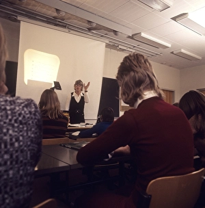 In the 1970s. A school class sits in the benches during a lesson with a female teacher