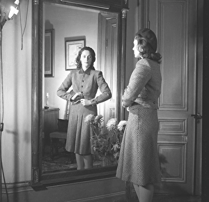 Actress Viveca Lindfors, 1920-1995. She stands in front of the mirror and buttons the last button of her plaid two-piece suit with a knee-length skirt and a waist-length jacket. 1945. Kristoffersson ref R55-6