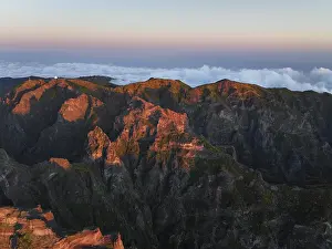 Aerial drone view of Pico do Arieiro and mountains over clouds on sunset