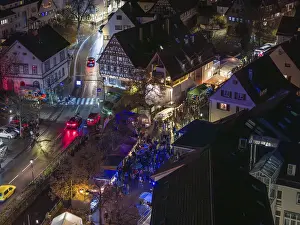 Aerial view of a busy Christmas market at night with illuminated half-timbered houses and crowds of visitors