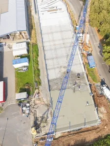 Aerial view of a construction site with blue crane and concrete surface next to a road