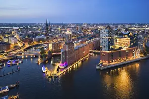 Aerial view of the Elbphilharmonie at blue hour with illuminated windows and view over the Speicherstadt and Hafencity