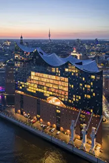 Aerial view of the Elbphilharmonie at sunset with illuminated windows and view over Hamburg