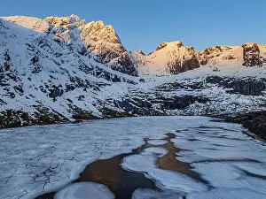 Aerial view of icy lake in front of steep mountains