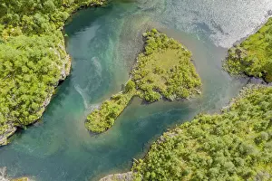 Aerial view of an island in a turquoise colored river surrounded by birch forest