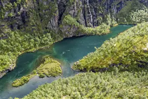 Aerial view of an island in a turquoise colored river surrounded by birch forest