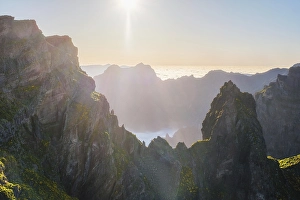 Category Mountain Landscapes Prints: Aerial view at Pico do Arieiro of mountains over clouds with blooming Cytisus shrubs on sunset with sunburst