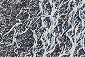 Aerial view, a red single-engine lightweight airplane flying over the flow structures of the melt water branching out