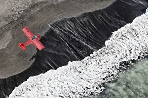Aerial view, a red single-engine lightweight airplane flying over the waves of the North Atlantic