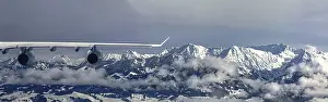 Category Mountain Landscapes Prints: An aeroplane flies over a snow-covered mountain landscape and misty forests