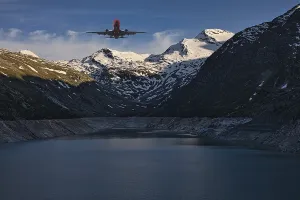 Aeroplane flying over a mountain lake with snow-covered peaks under a blue sky