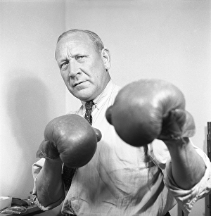 Age is just a number. An older man in a shirt and tie wears boxing gloves and he stands as a boxer should, with his guard up to block a punch but at the same time ready to strike