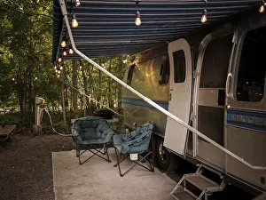 An Airstream camper trailer with string lights and chairs set up in a forest