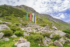 Alpine landscape with colourful flags and a sign next to piles of stones