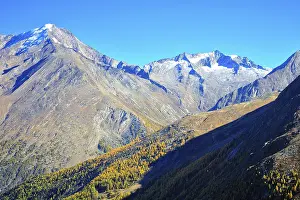 Alpine landscape with snow-capped peaks and autumn trees under a blue sky