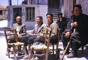 Alte Maenner sitzen vor einem Dorfcafe und trinken Kaffee, junge Maenner im Hintergrund, Zypern 1963