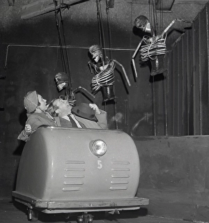 Amusement park in the 1950s. A couple passes skeletons in an amusement park ride