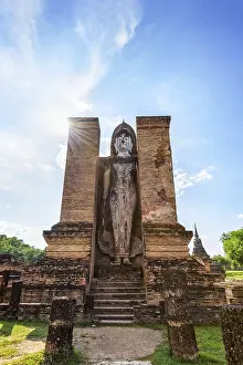 Ancient Buddha statue stand posture under the blue sky among the ruins of Wat Maha That temple at Sukhothai Historical
