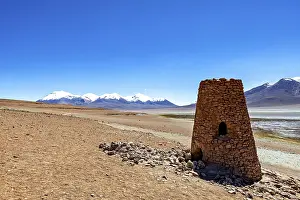 Ancient stone structure in a vast desert landscape with snowy mountains in the background